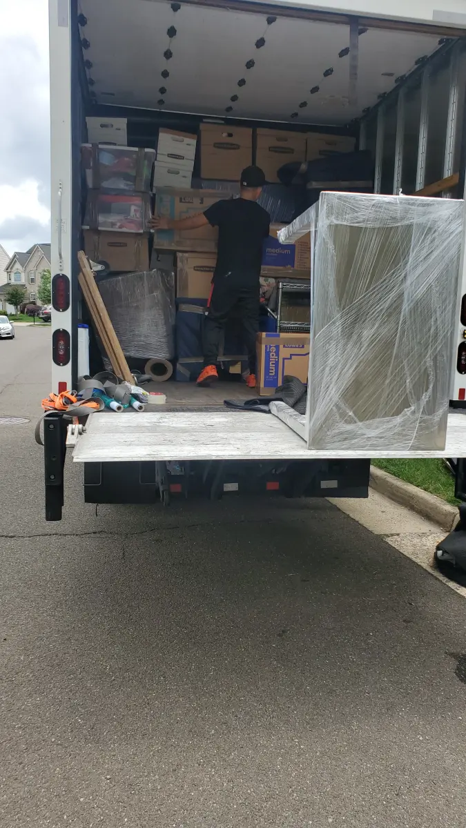 M.C. Movers crew member loading boxes and shrink-wrapped furniture into a moving truck