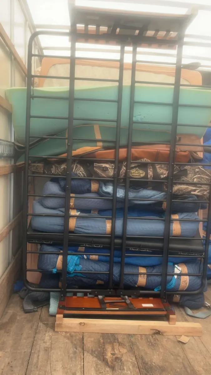 Furniture wrapped in moving blankets and secured behind a bed frame in an M.C. Movers truck