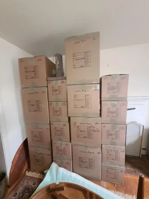 Boxes packed and labeled by room, stacked in a living room by M.C. Movers