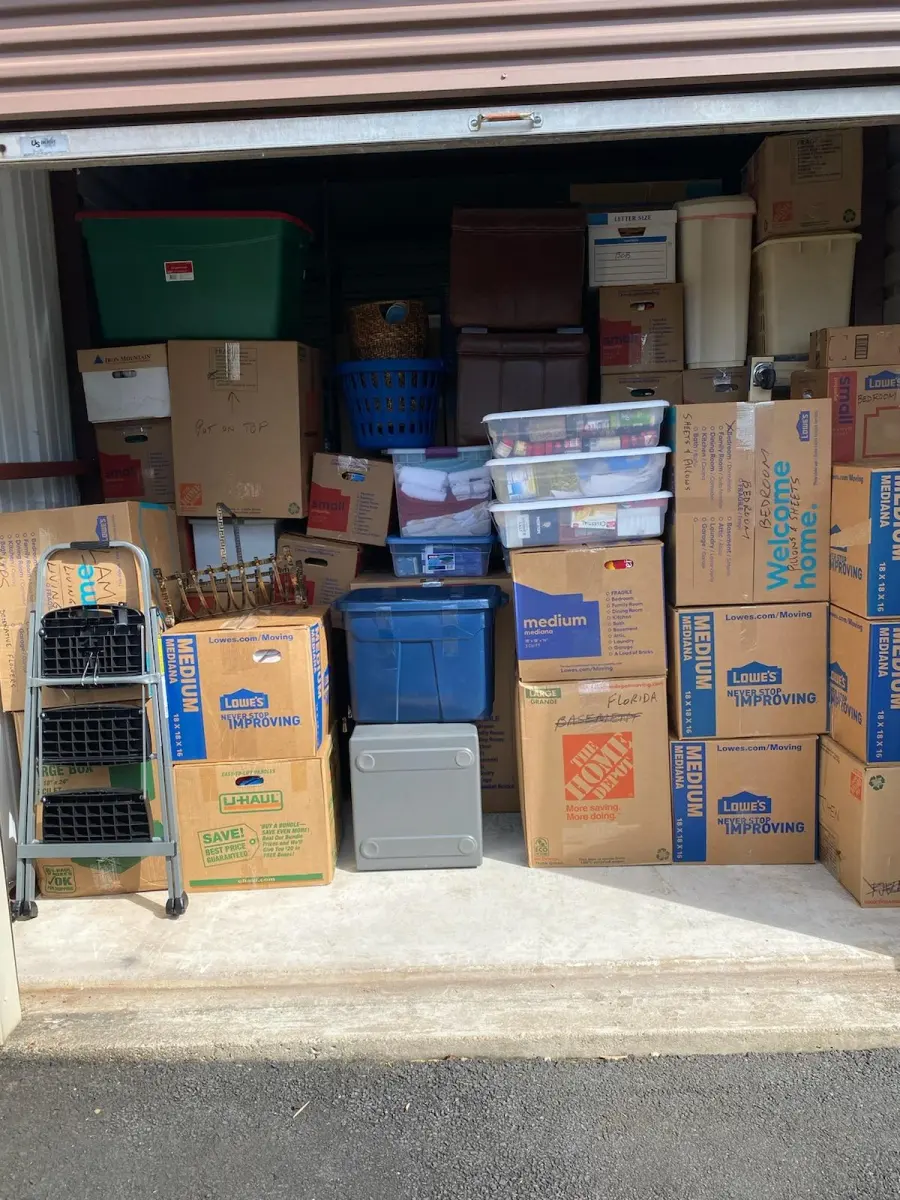 Storage unit neatly packed with labeled moving boxes and bins by M.C. Movers